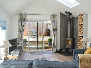 COSY LOUNGE AREA WITH WOOD BURNER & PATIO DOORS LEADING TO THE DECKING AREA